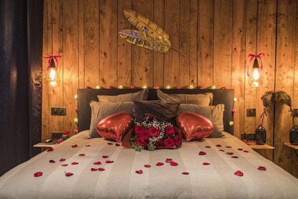 Lit décoré avec des pétales de rose et coussins en forme de cœur dans une love room chaleureuse