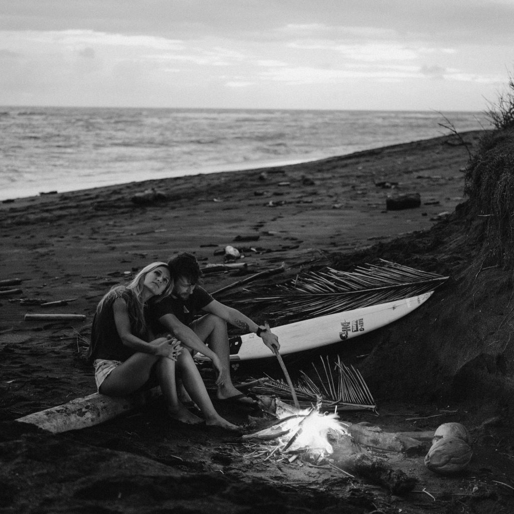 Couple profitant d’une soirée sensuelle sur la plage autour d’un feu, ambiance romantique et sauvage.