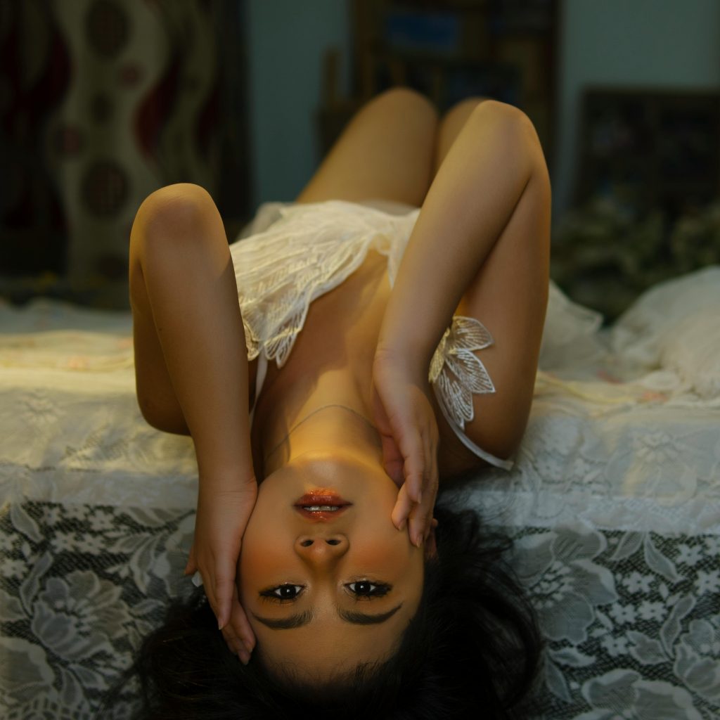 Femme en lingerie blanche dans une position sensuelle sur un lit, ambiance propice aux préliminaires sensuels