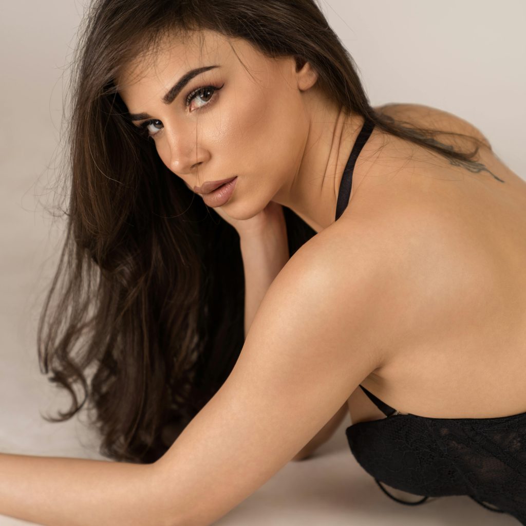 Femme brune en lingerie noire, regard vers l’objectif, posture élégante et sensuelle