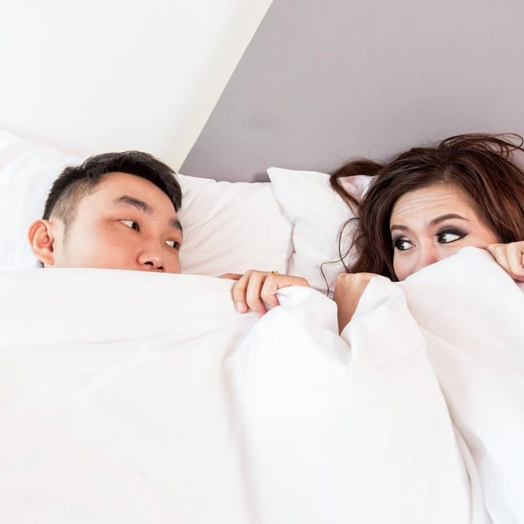 Couple allongé dans un lit, partageant un instant complice dans une love room romantique à Toulouse.