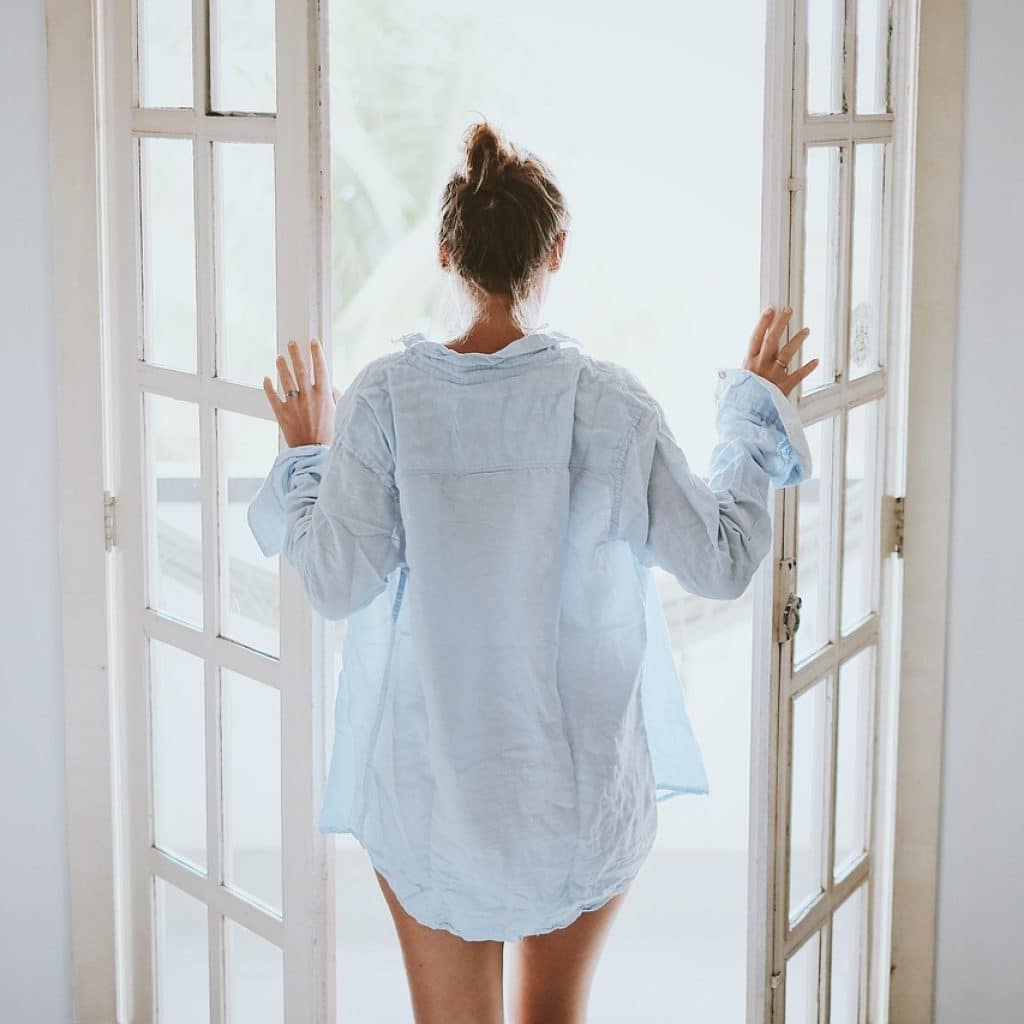 Femme ouvrant les portes-fenêtres d'une chambre lumineuse en week-end amoureux à Toulouse