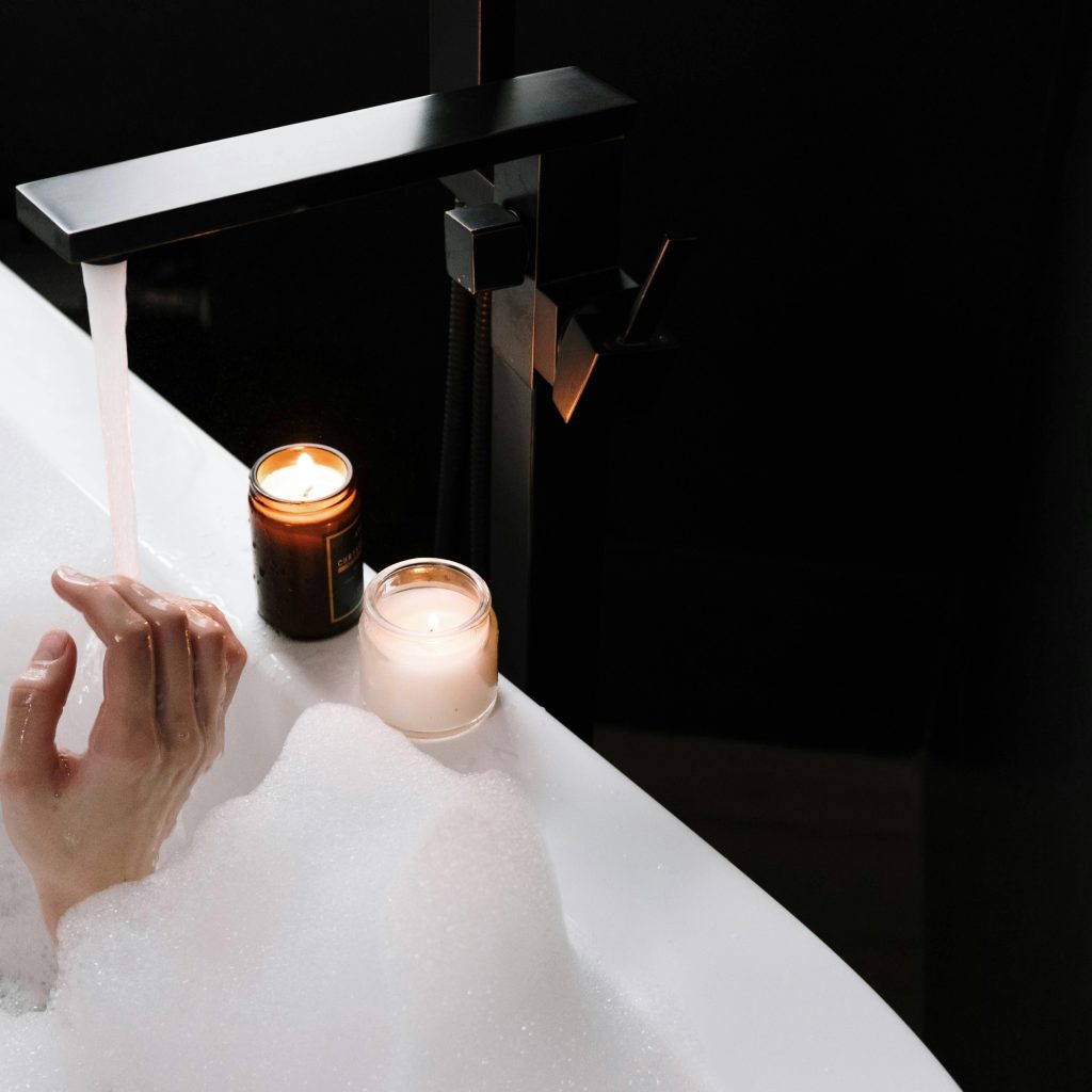 Main dans l’eau d’une baignoire moussante avec bougies allumées, détail d’un moment intime en love room ou hôtel romantique à Toulouse.