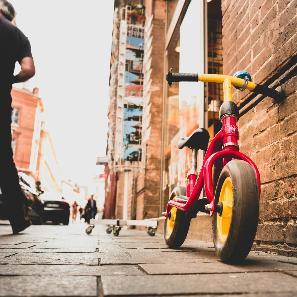 Vélo d’enfant rouge et jaune posé contre un mur en centre-ville, atmosphère authentique proche des love rooms lors d'un Week-end amoureux Toulouse