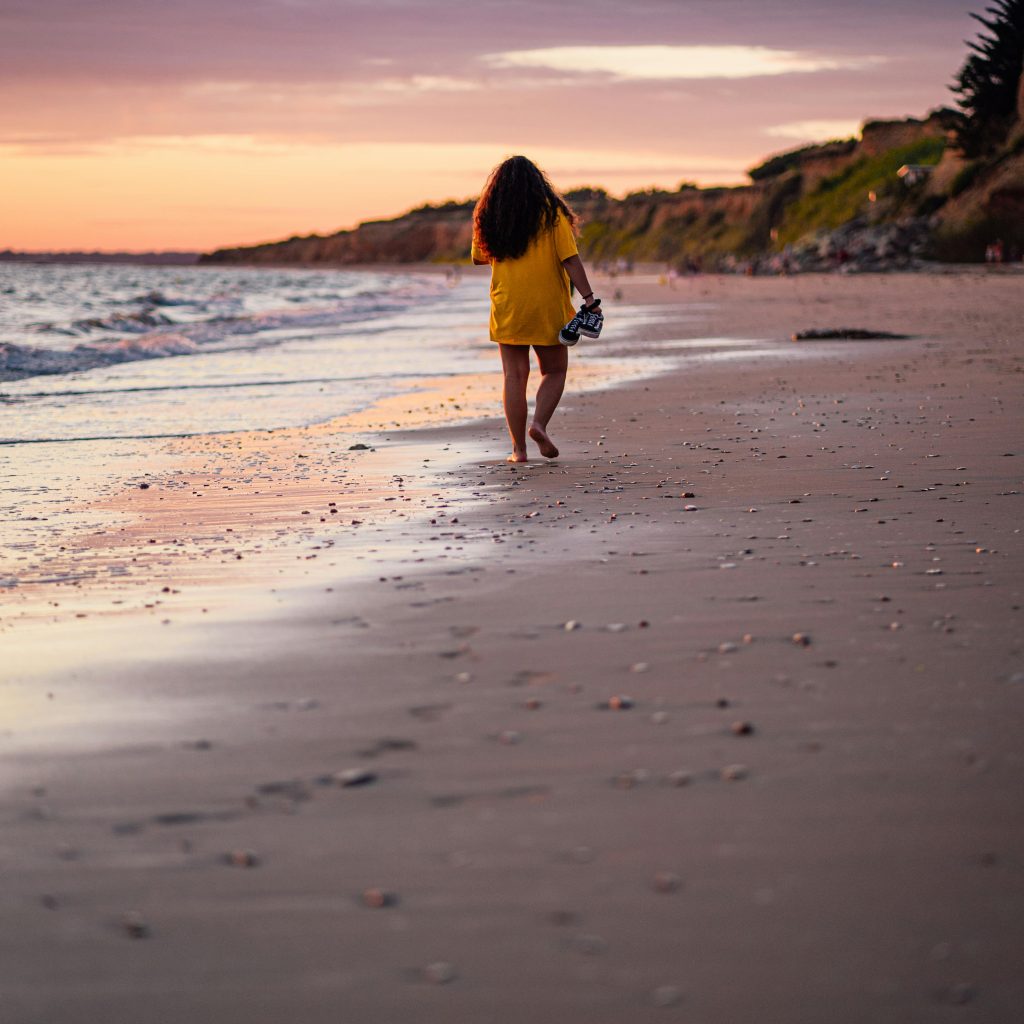 Femme marchant sur la plage au coucher du soleil en Bretagne sud, un instant de sérénité et de romantisme lors d'un week-end en amoureux.